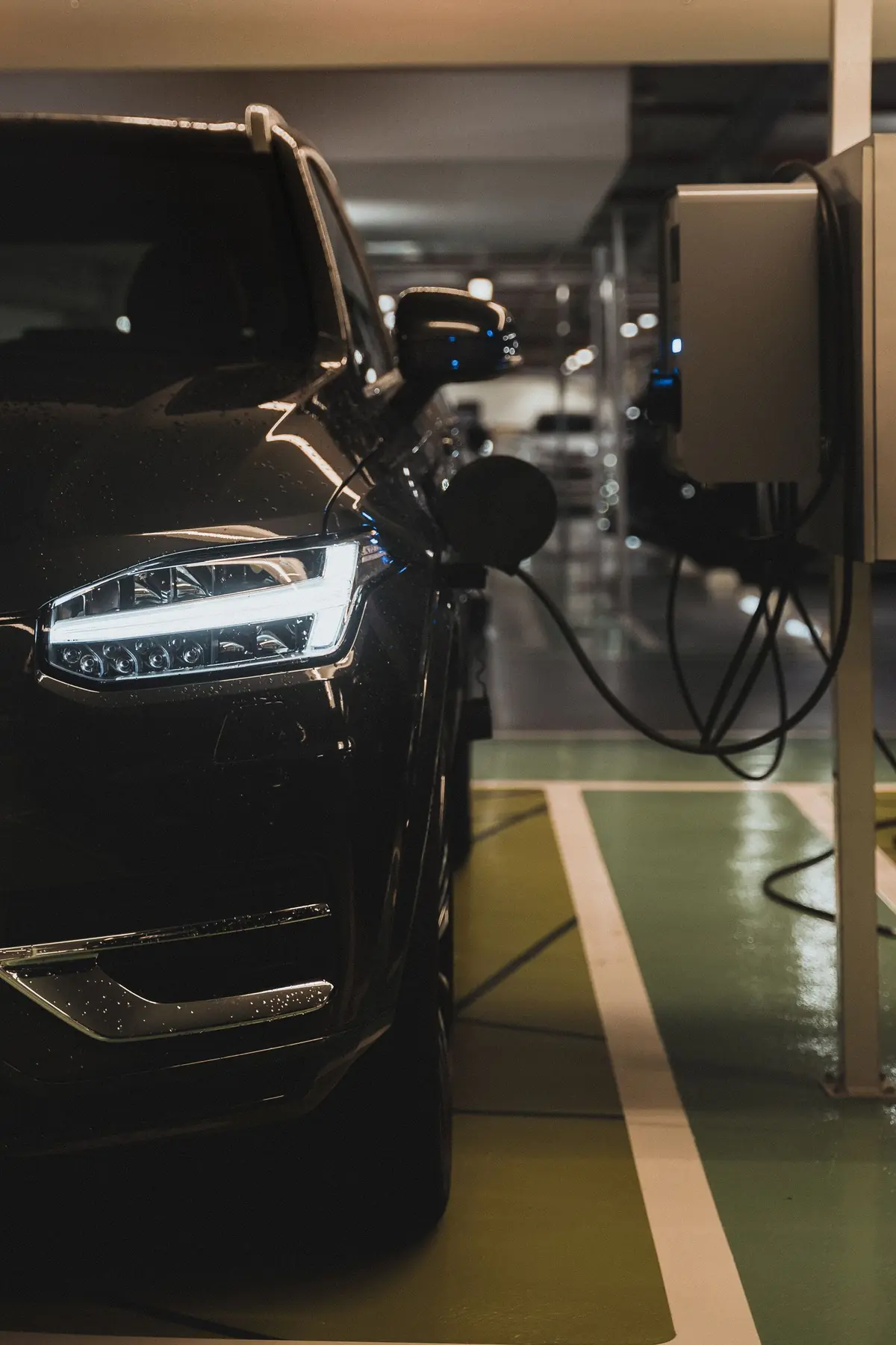 Voiture électrique en charge sur une borne murale dans un parking, phares allumés